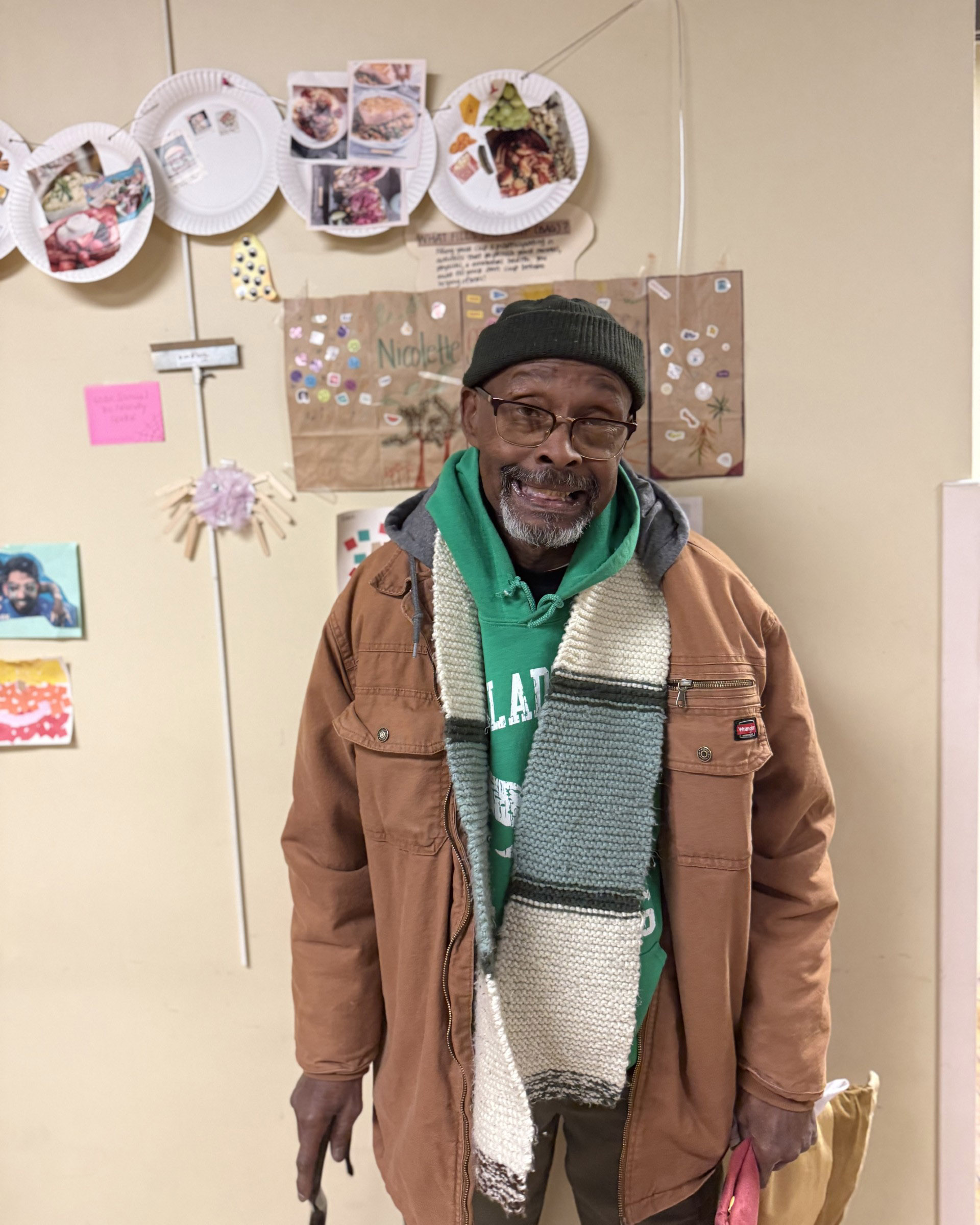 A man smiles in front of a wall decorated with handmade art