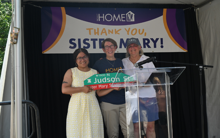 Three women holding a street sign.