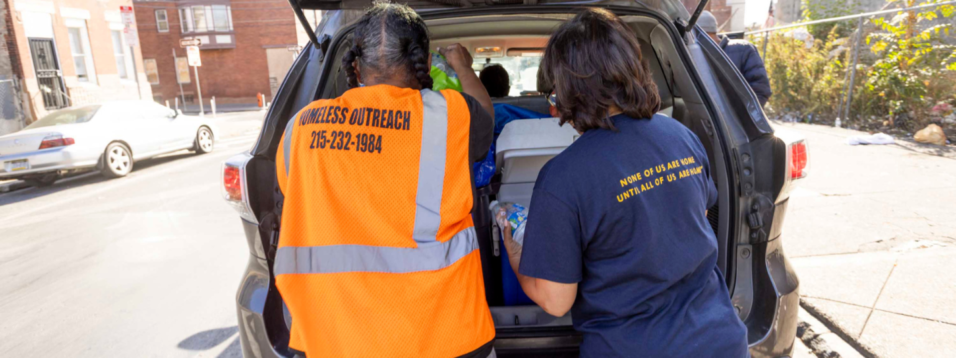 Two women working street outreach gather water bottles