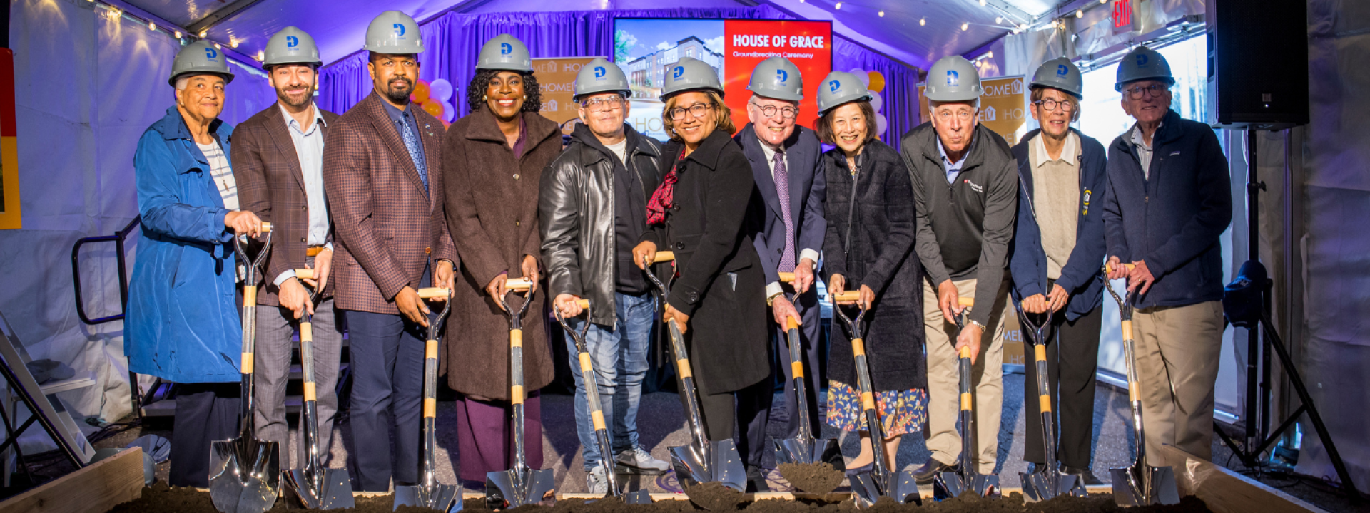 A group of people holding shovels in dirt, smiling