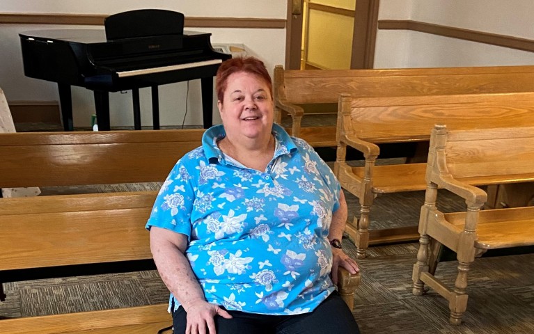 Linda, a resident of Project HOME sitting on a wooden pew in Kate's Place, Project HOME's largest residence in Center City.