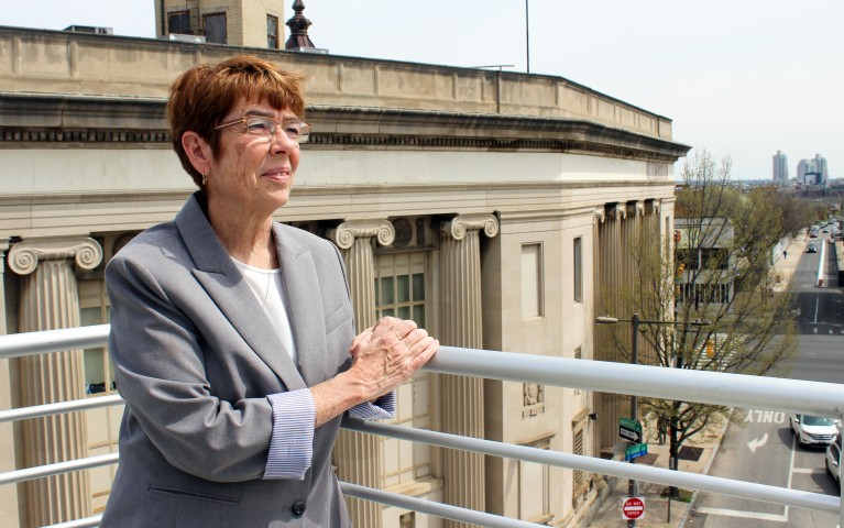 Project HOME Co-Founder Sister Mary Scullion rests her hands on a railing on top of our JBJ Soul Homes building with the view of the city of Philadelphia behind her. 