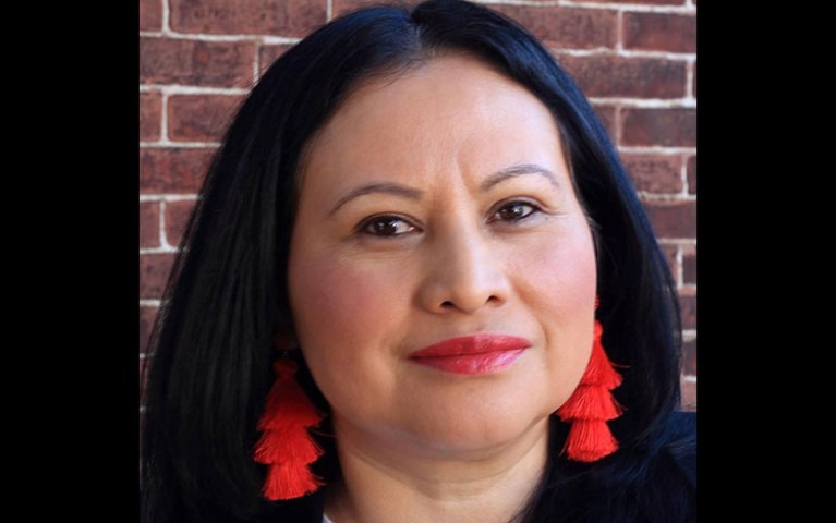 A head shot of a woman with dark hair, red earrings and a warm smile. 