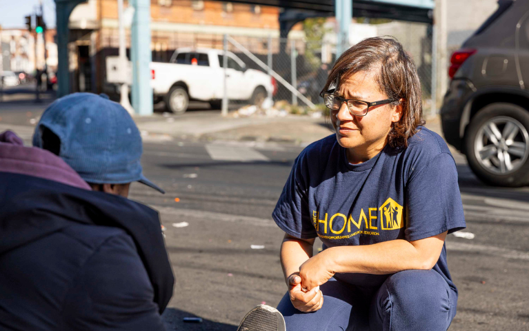 A woman crouching and speaking to another woman sitting on sidewalk