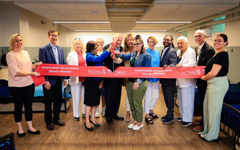 A line of people holding a red ribbon, with two of them cutting in with giant scissors.