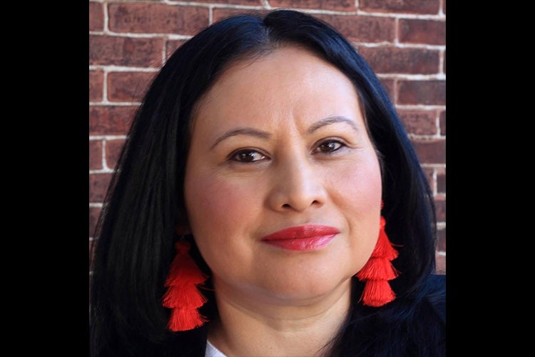 A head shot of a woman with dark hair, red earrings and a warm smile. 