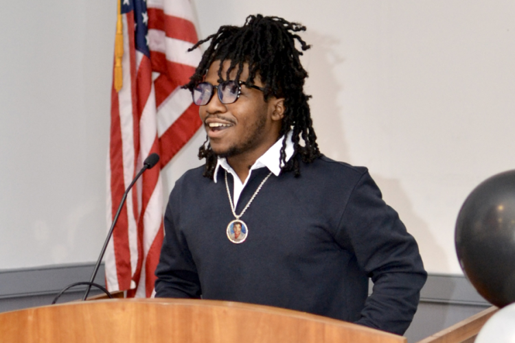 Hamin Muhammad smiles while speaking at a podium in front of an American flag at Project HOME's Honickman Learning Center Comcast Technology Labs